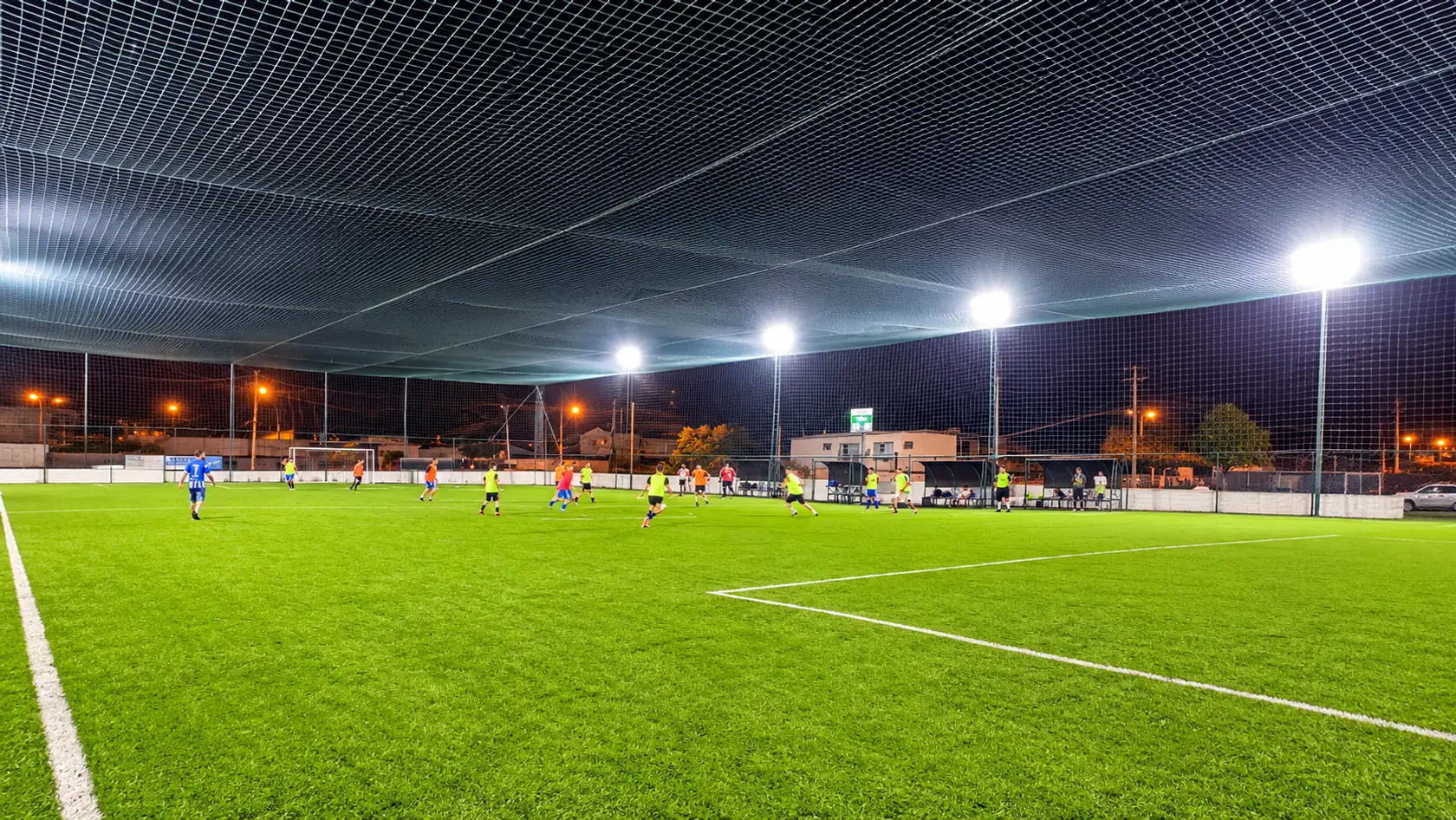 Jogo noturno no campo de futebol society da Arena Europa, com o gramado iluminado pelos refletores